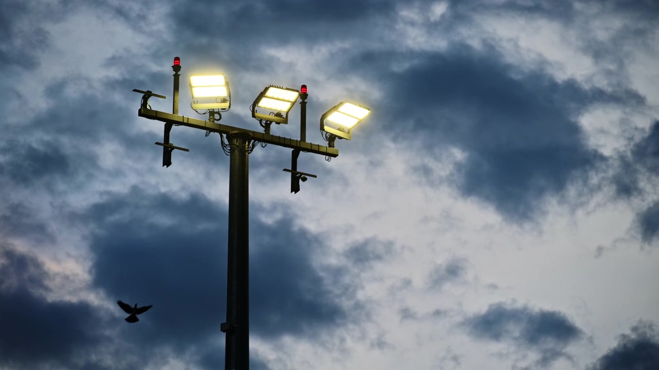 Zicht op een hoge schijnwerpermast met brandende lampen en rode waarschuwingslichten tegen donkere stormwolken, Praag, Tsjechië.