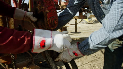 unrecognized men wearing large protective gloves arrange the equipment for oil drilling. workers hang the metal clips on the hook.