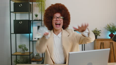 cheerful rich business woman working on office laptop, wasting throwing money to camera, profit, win