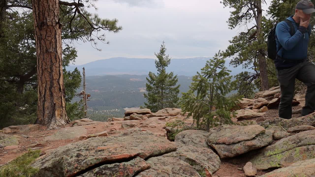 One male hiker walks back from a remote mountain overlook in windy conditions. Filmed in Staunton State Park during the spring.