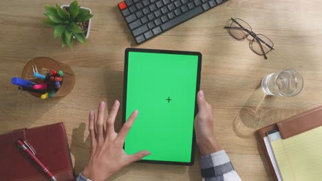 vista de arriba hacia abajo de una computadora portátil con pantalla verde simulada pantalla chromakey en un escritorio de oficina de madera al lado de la libreta con bolígrafos, gafas y un vaso de agua.