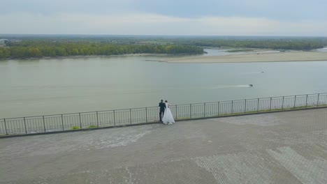 newlywed couple looks at calm river from hill bird eye view