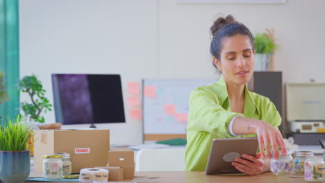 woman with digital tablet running online business making candles at home