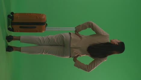 full body of back view asian businesswoman traveler with luggage standing with arms akimbo in the green screen background studio, during sunset time