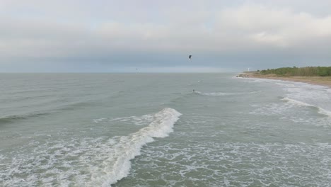 establishing aerial view of a group of people engaged in kitesurfing, overcast winter day, high waves, extreme sport, baltic sea karosta beach , distant drone shot moving forward