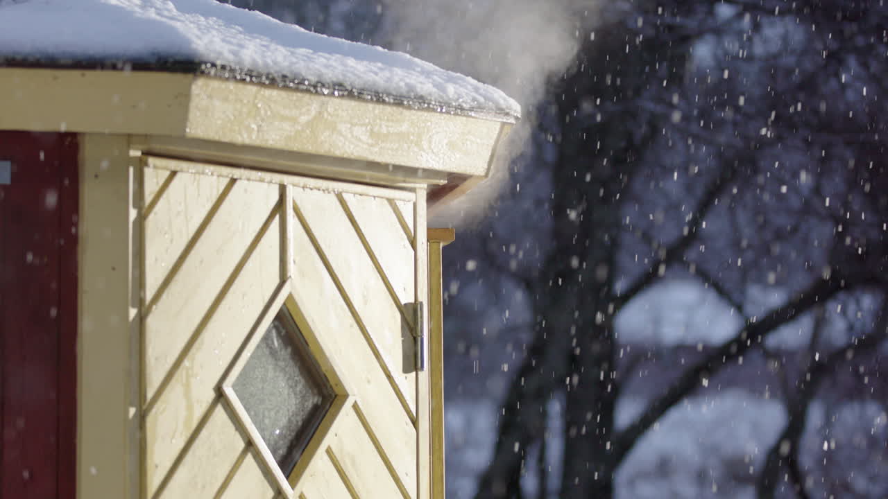 Steam escapes from wooden wood-fired sauna as snow falls, telephoto