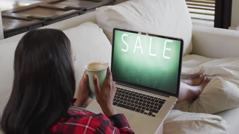 biracial woman using laptop on couch at home online shopping during sale, slow motion