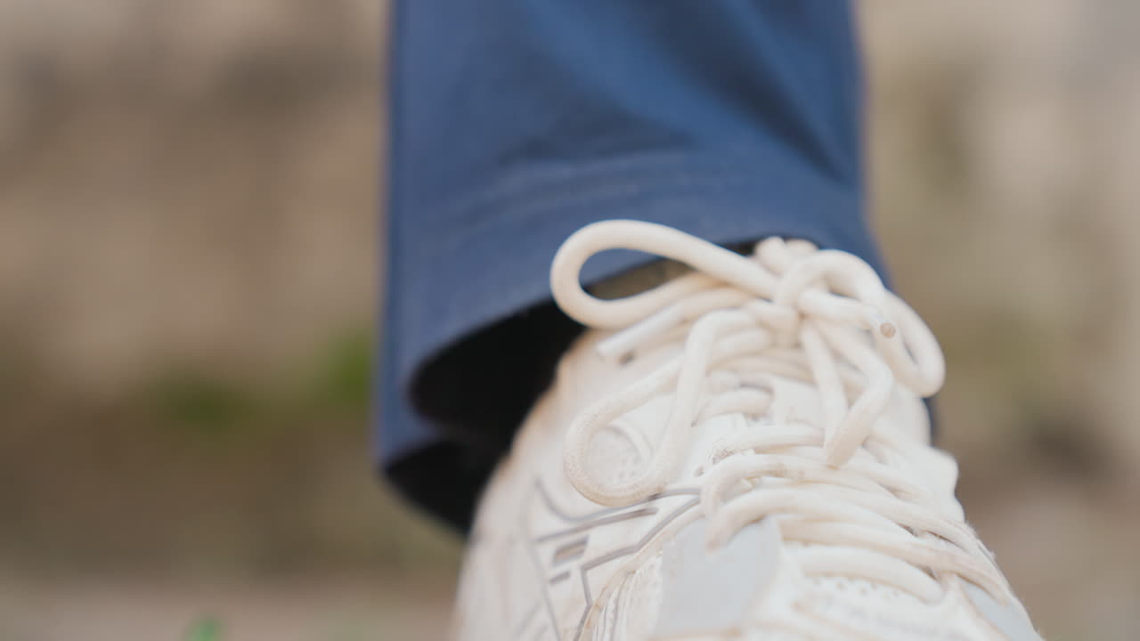 Lacci allacciati su sneaker bianca in primo piano che mostra un nodo ben fatto sotto l'orlo di un pantalone blu scuro, piede in posizione e pronto a muoversi, sfondo morbido, dettaglio focalizzato, preparazione quotidiana e tranquilla attesa.