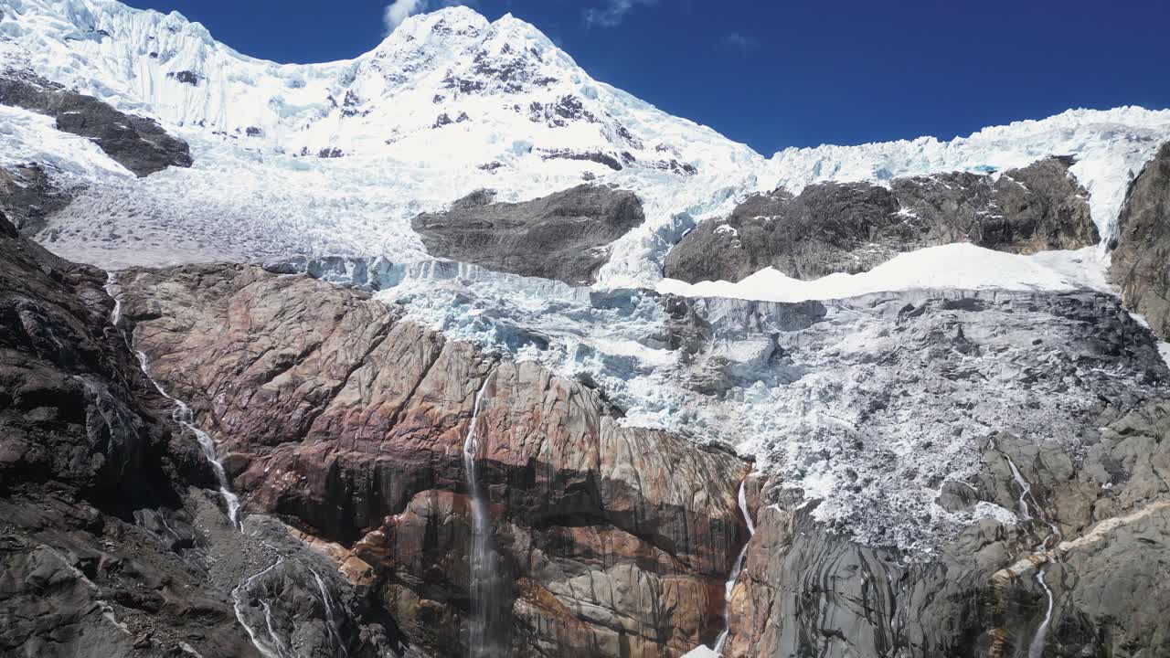 Aerial rises over mountain peak glacial waterfalls on rock cliff, Peru
