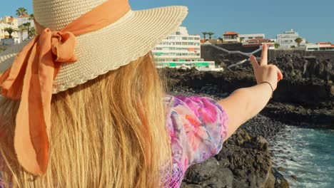 beautiful woman with hat showing peace sing, puerto de santiago in background