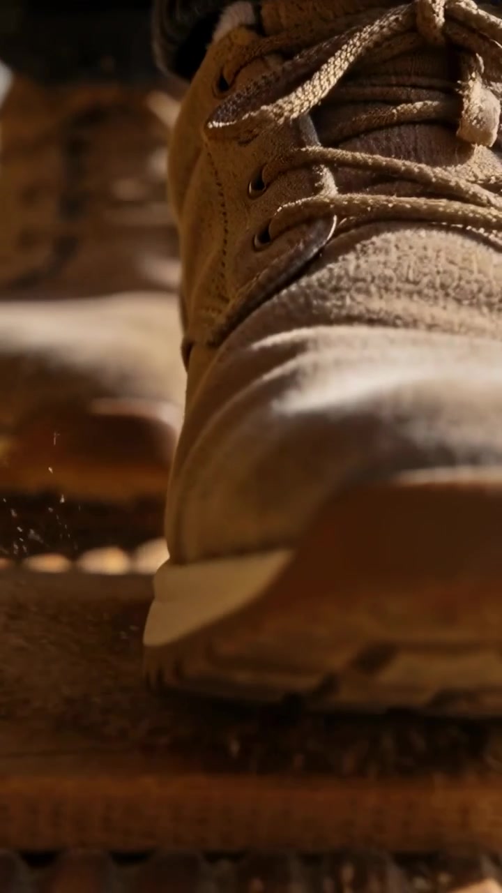 Video verticale: Una scarpa da ginnastica marrone con calzino grigio viene appoggiata su doghe di legno, spargendo polvere.