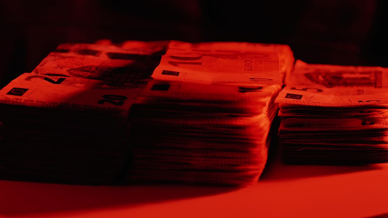 Rotating stack of Euro notes lit in red light to evoke economic danger, secrecy
