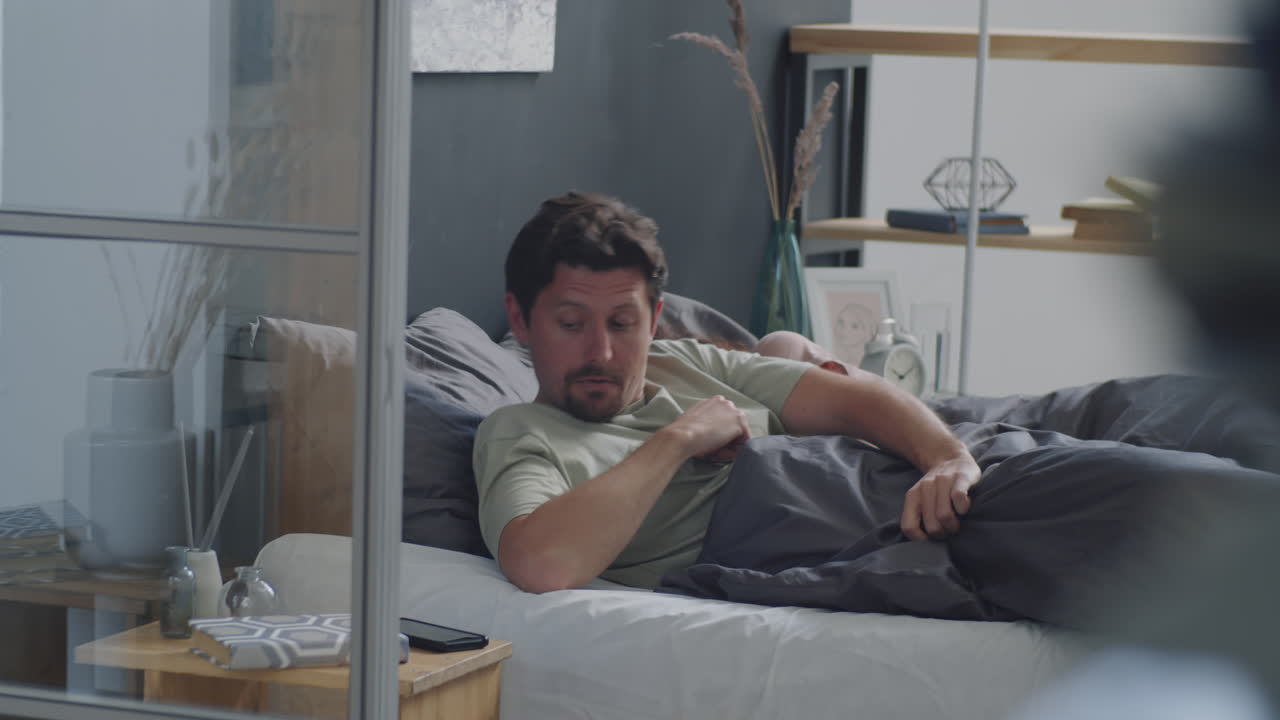 침대에 있는 커플, 전화를 확인하는 남자