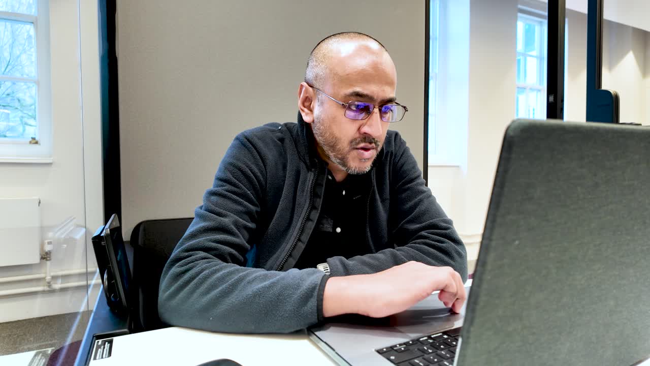 South asian office worker with glasses focusing on the information displayed on his laptop