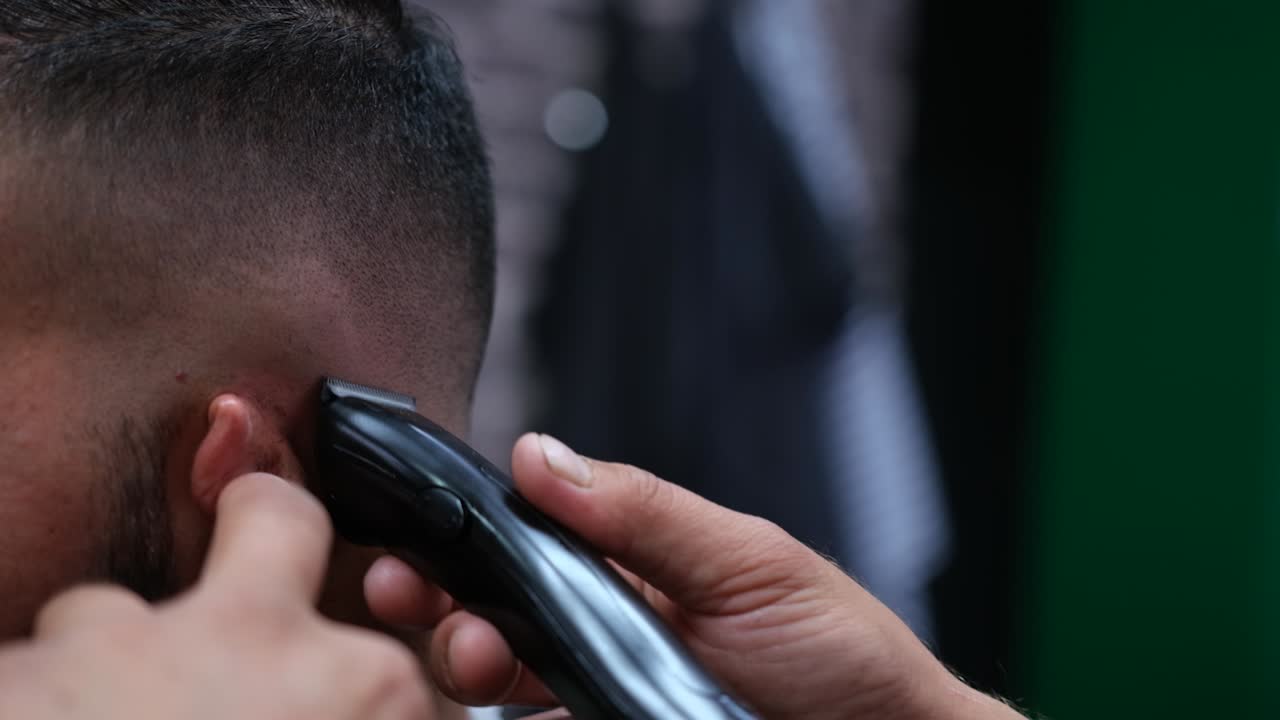 primer plano de un barbero usando una afeitadora eléctrica para darle a un cliente masculino un atajo