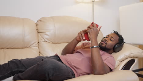 Man relaxing on couch with headphones and phone