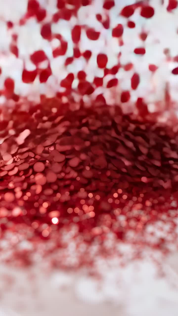 Vertical video: Dropping red sequins from above onto white surface, forming shimmering mound
