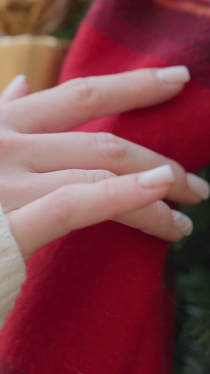 Close-up of woman hand in white sleeve gently touching large Christmas tree ornament, with festive tree decorations in soft focus and holiday spirit in the background