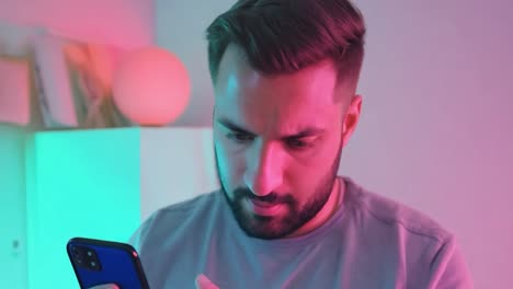 un joven está usando un teléfono inteligente en una habitación iluminada con luces led de colores. está deslizando, tocando y viendo contenido en su teléfono