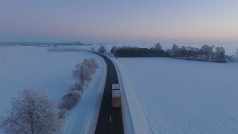toma aérea de establecimiento de un paisaje rural, camino rural con camiones, campos agrícolas y árboles cubiertos de nieve, clima helado, luz de la hora dorada, toma amplia de drones que avanzan