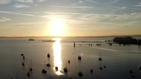 boats silhouetted on golden shimmering harbour ocean surface aerial view dolly left