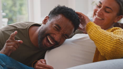 pregnant couple on sofa at home with man listening to woman's stomach