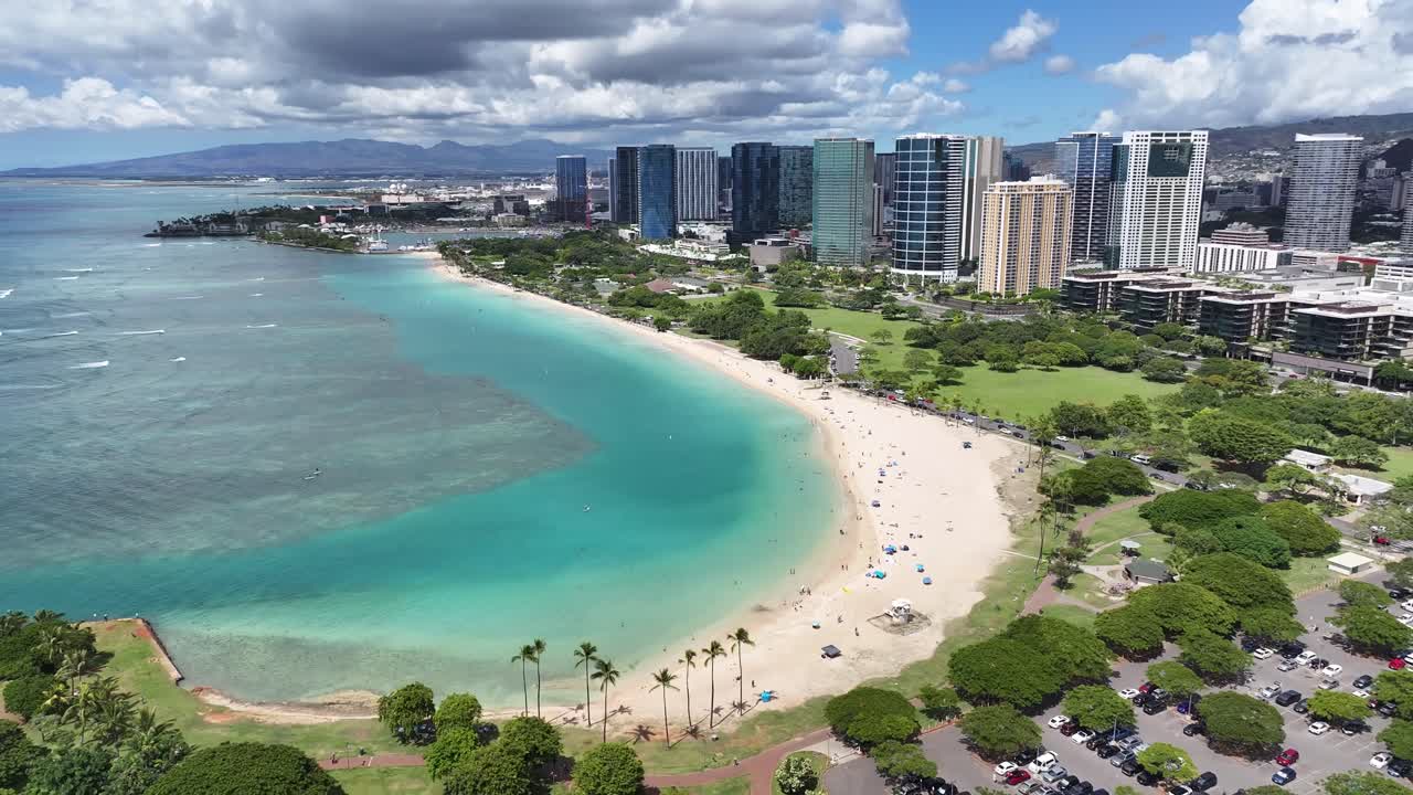 Aerial drone footage of tropical Waikiki Beach in Honolulu, Oahu, Hawaii, showing turquoise ocean waves, palm trees, and hotels along the coastline