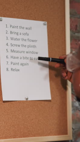 Black man with goggles reads housework to-do list on cork board near brick wall closeup. African-American worker study plan of repair stages