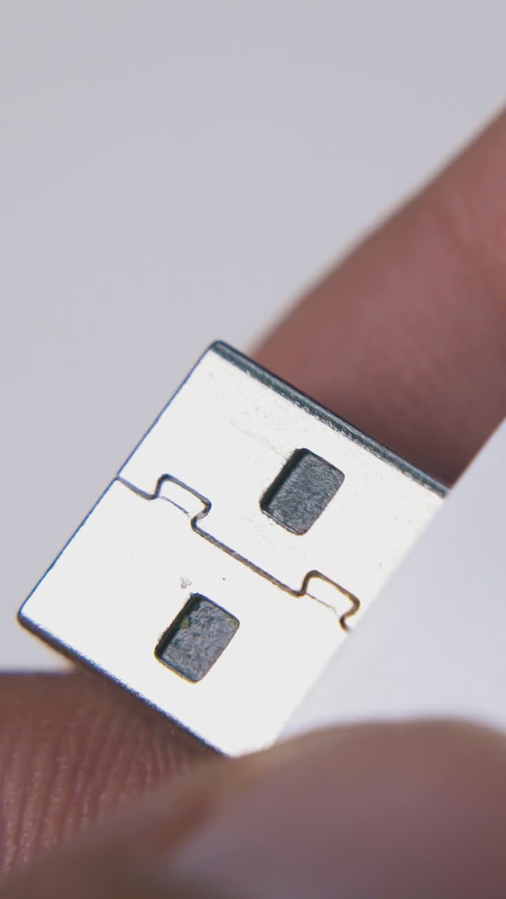 young man examines modern memory stick in white and orange case on light background extreme close view