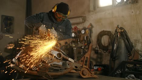 locksmith sands the decorative metal steampunk fish sculpture by electric grinder with a lot of sparks in slow motion, metalwork at workshop, 4k 60p prores hq