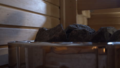 water pouring over steamy rocks of wood stove in finnish sauna, close up shot