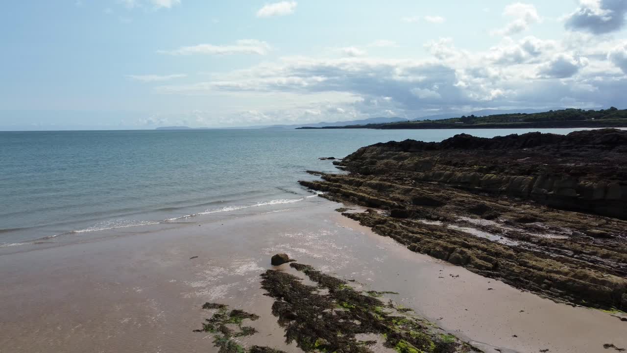 Aerial view Traeth Lligwy Jurassic rocky weathered rugged Anglesey shoreline, pull back shot