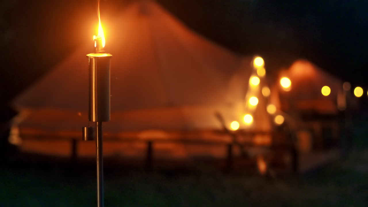 Tende con torce accese, lampade e sedie di legno al glamping, foresta circostante, notte