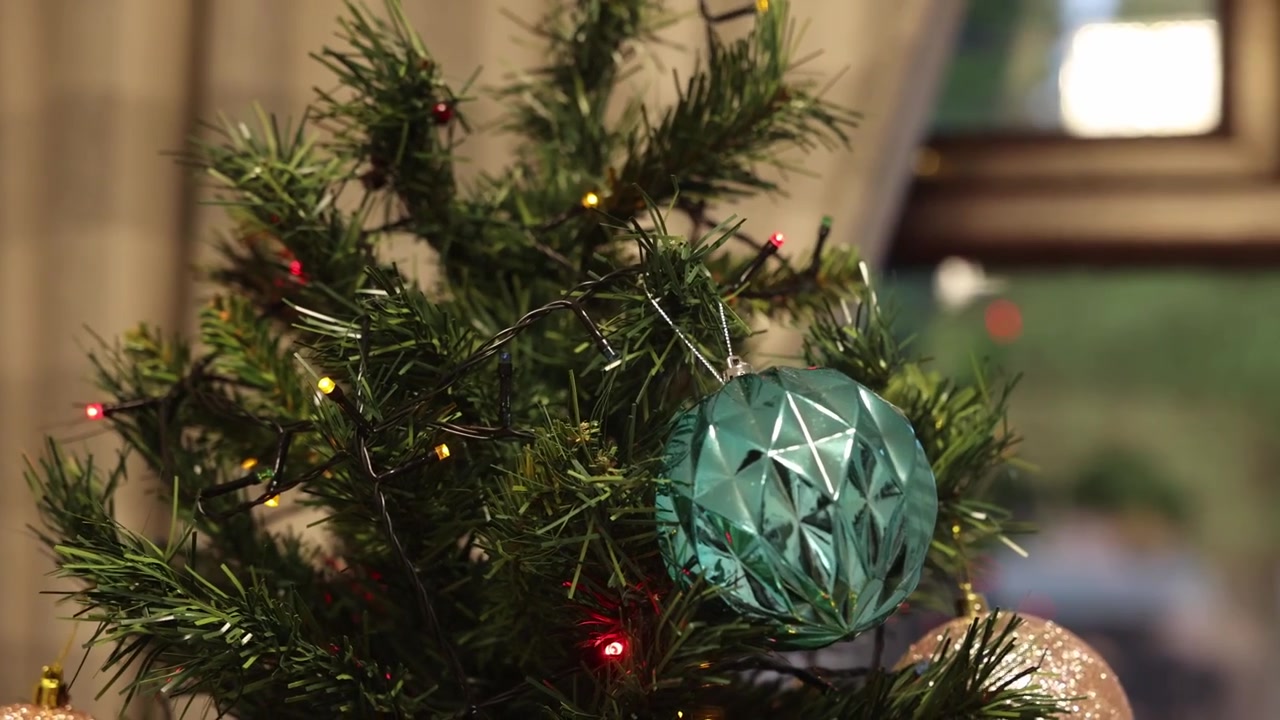 Close-up de uma mão colocando enfeites nas ramagens da árvore de Natal como decoração.