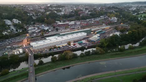 Drohnenflug-Am-Frühen-Morgen-über-Den-Bahnhof-Von-Exeter-Saint-David-Und-Blick-Auf-Die-Stadt,-Luftbild-Rückwärts-Vor-Sonnenaufgang,-Einschließlich-Fluss-Exe-Und-Hochwasserkanal