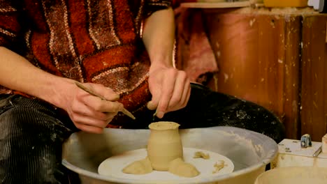 professional potter carving mug with special tool in pottery workshop