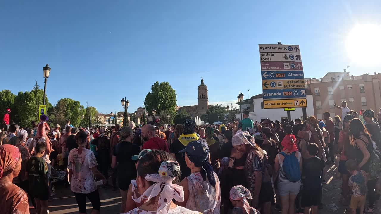 Guadix Festival of Cascamorras 2024. Crowd of people covered in colors dancing and jumping in frotr of the cathedral.