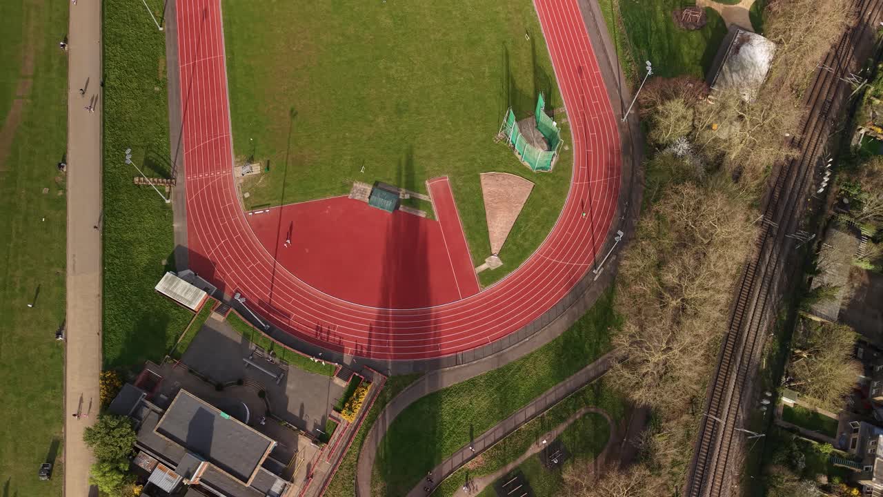 Aerial view looking down over runner on red running track in Parliament hill London oval landmark
