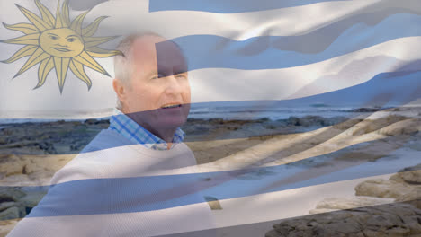 animation of flag of uruguay over happy senior caucasian man on beach
