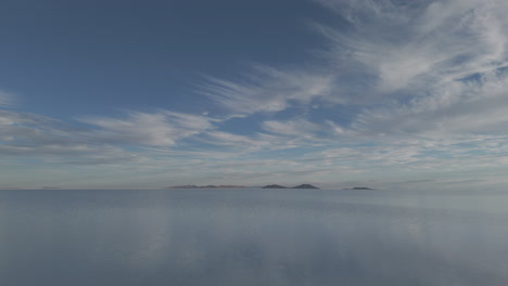 drone shot flying above the mirror salt flats in bolivia uyuni on a cloudy day with the visible reflection log