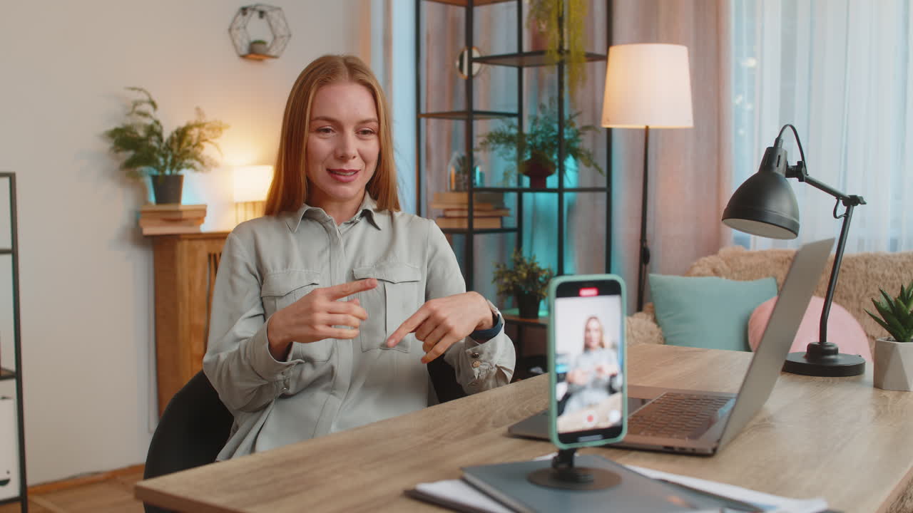Una donna d'affari sorridente registra un webinar di formazione sulla motivazione su una webcam tramite smartphone in ufficio a casa