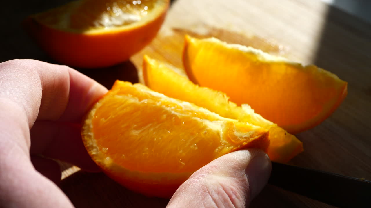 cortar una rodaja de fruta naranja madura con un cuchillo a la luz del sol en una tabla de cortar para un refrigerio saludable