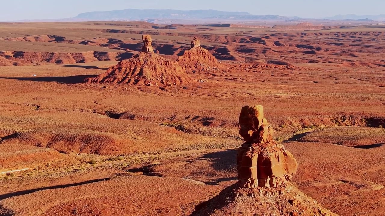 Drone pushes toward a sandstone formation at Valley of the Gods, Utah, with Rooster Butte and vast red desert beyond