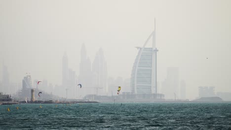 Vista-Panorámica-Del-Horizonte-De-Dubai-Y-El-Burj-Al-Arab-Mientras-Los-Kitesurfistas-Disfrutan-Del-Día-En-La-Playa-De-Fazza