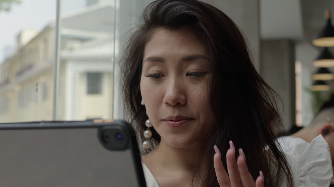 커피숍에서 태블릿으로 전화 회의를 하는 젊은 아시아 여성