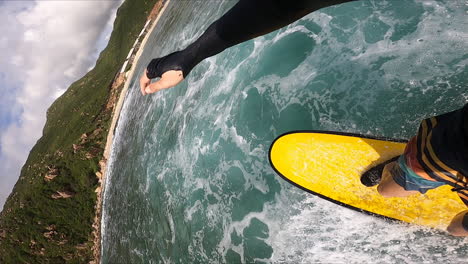 vertical shot - surfer on a yellow surfboard surfing towards the coast on mexican bay in summer