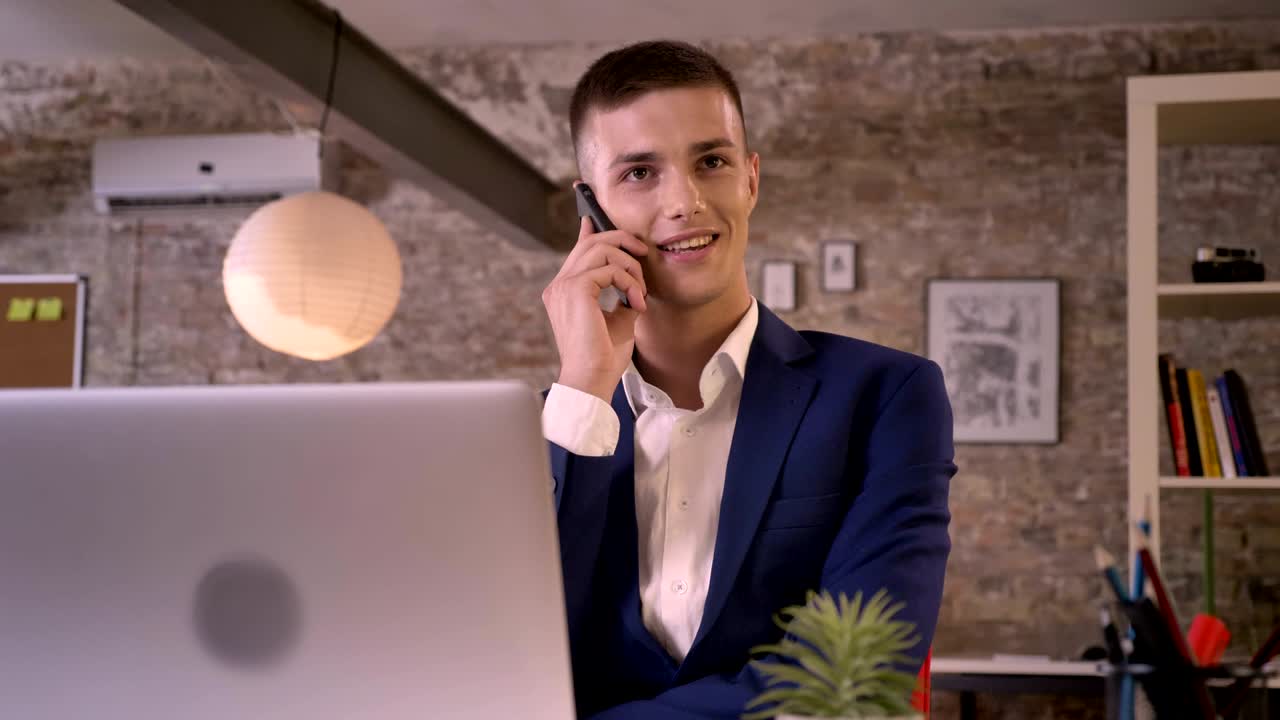 Young attractive businessman is talking on smartphone, working with laptop, communication concept, business concept
