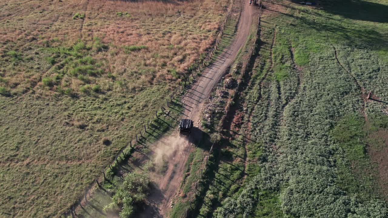 Drone captures an ATV racing through a winding dirt path between open green fields in Costa Rica.