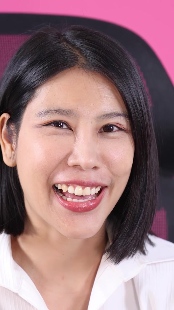 Confident businesswoman smiles and talks in closeup portrait, seated on office chair, pink background