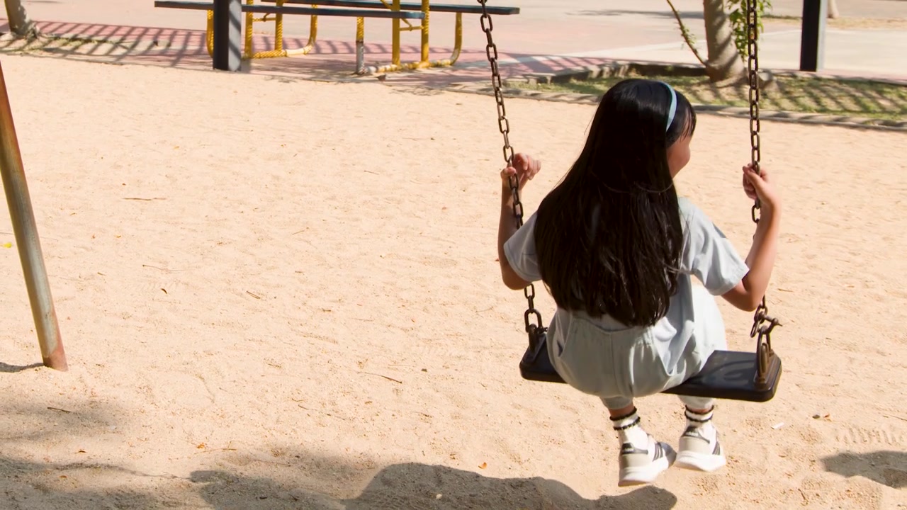 Una giovane ragazza in salopette si diverte a dondolarsi in un parco giochi all'aperto nel Parco Lumpini, Bangkok